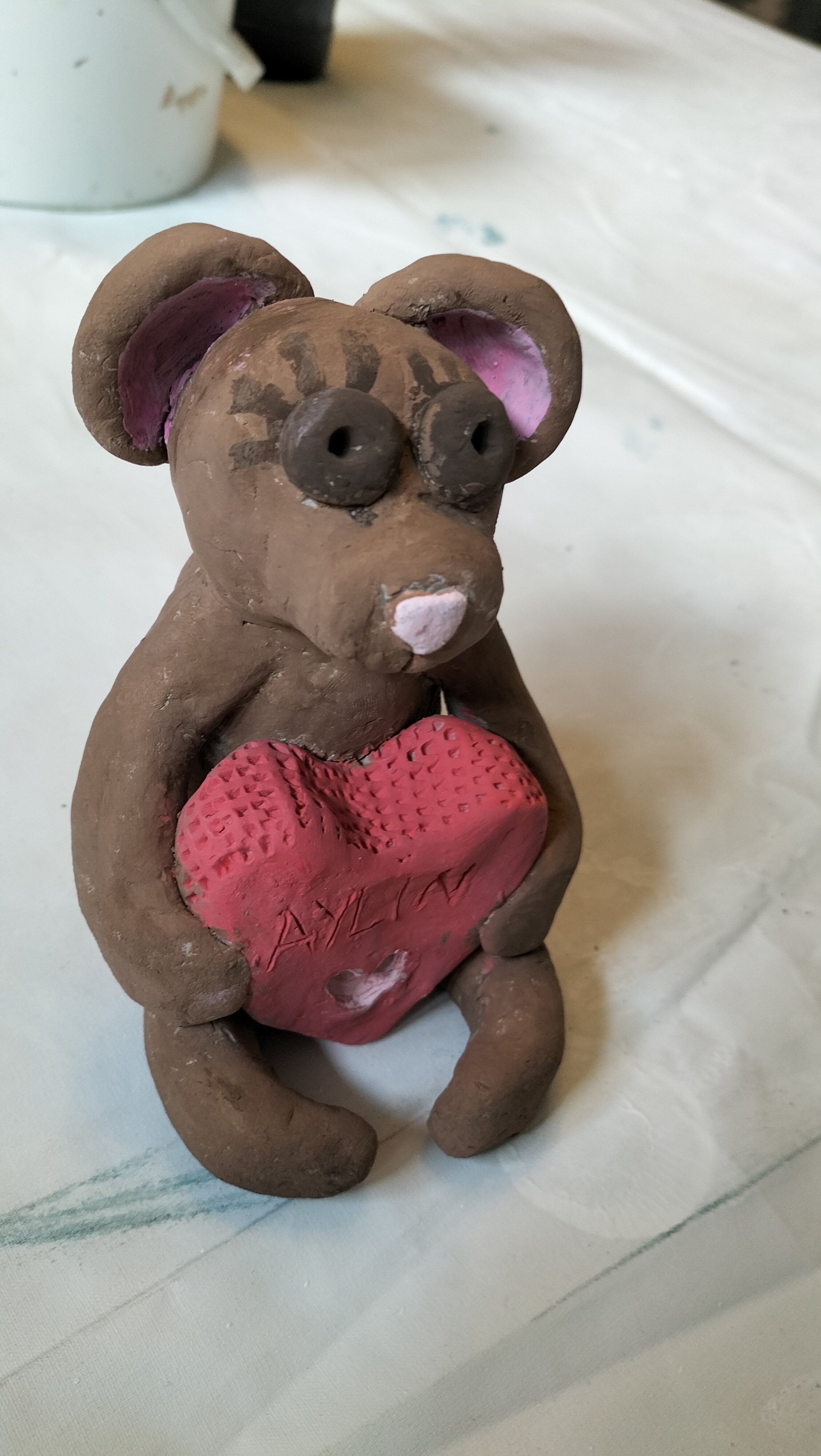 Braune Tonmaus mit rosa Ohren haelt ein rotes Herz mit dem Namen Aylin